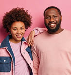 Photo of friendly happy woman and man with dark skin stand closely, smiles happily, wear fashionable pastel clothes, look at camera positively, isolated on pink background. Afro American couple